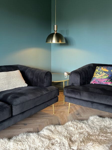 Cosy corner with velvet sofas, brass pendant light and teal walls in a sitting room designed by Megan Ace Interiors