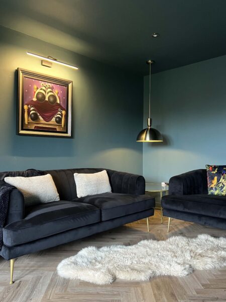 Cosy corner with velvet sofas, brass pendant light and teal walls in a sitting room designed by Megan Ace Interiors