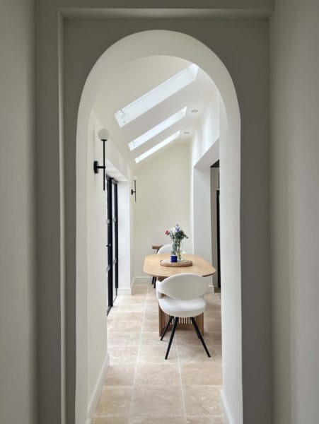 Contemporary dining area with round wooden table, boucle chairs, and black-framed glazing designed by Megan Ace Interiors