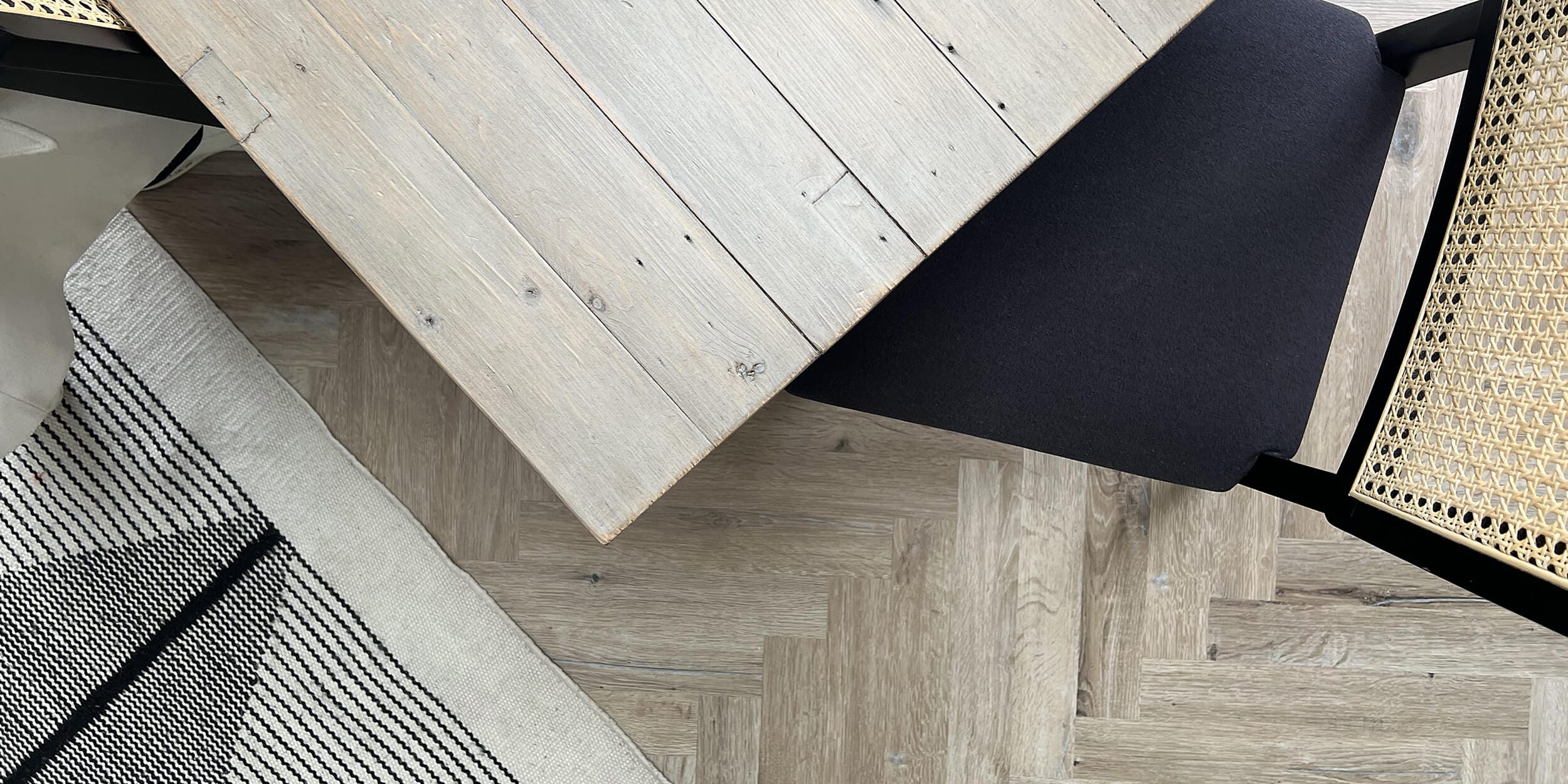 Dining area detail with oak herringbone floor, cane chair, and neutral woven rug by Megan Ace