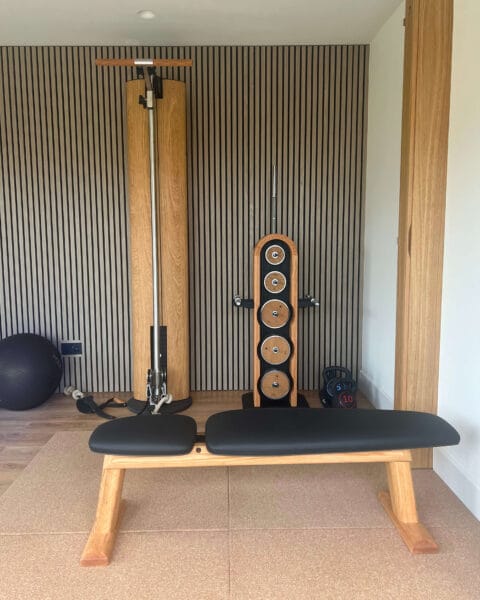 Modern home gym in Worcester with slatted wood wall and oak-framed fitness equipment designed by Megan Ace Interiors