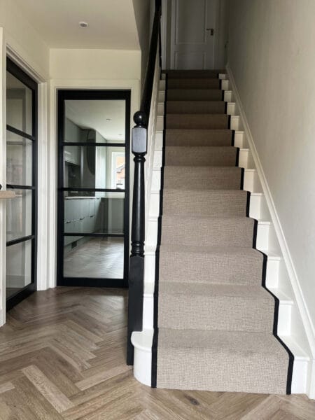 Hallway with herringbone flooring and neutral stair runner in a Worcester home designed by Megan Ace Interiors