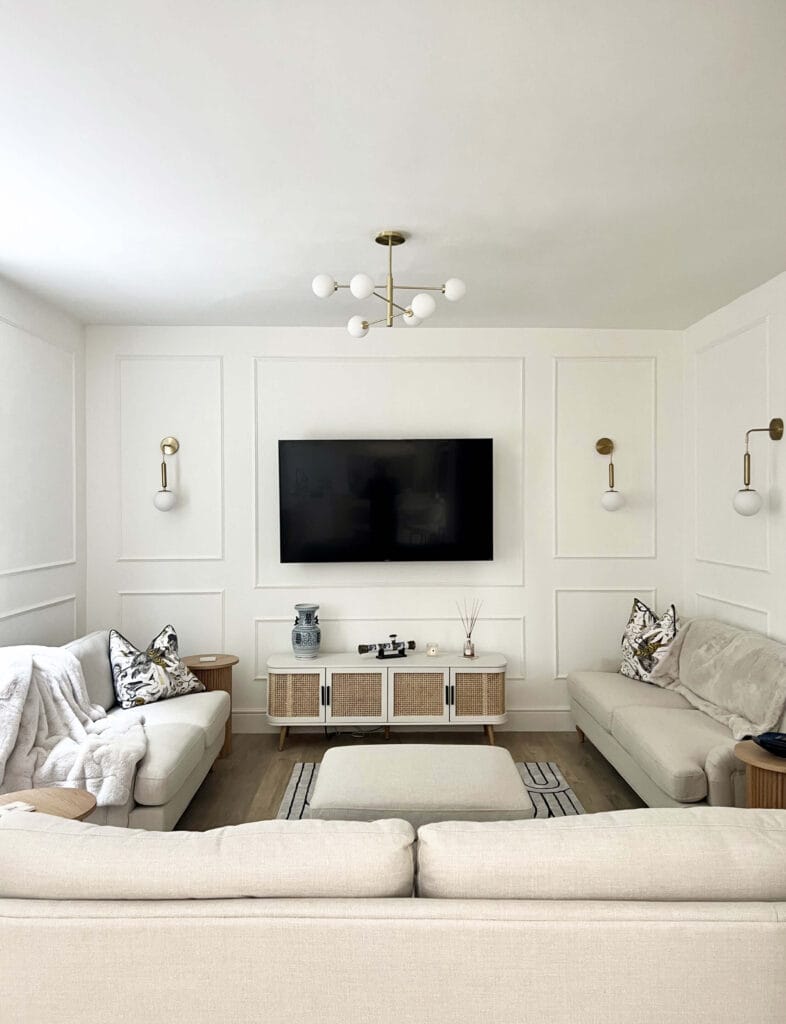 Contemporary living room with soft beige sofas, panelled walls, and brass light fittings by Megan Ace