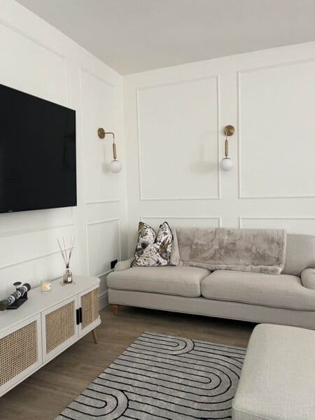 Contemporary living room with soft beige sofas, panelled walls, and brass light fittings by Megan Ace