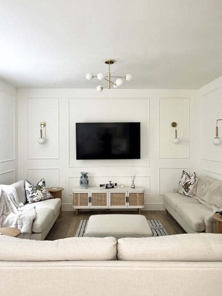 Contemporary living room with soft beige sofas, panelled walls, and brass light fittings by Megan Ace